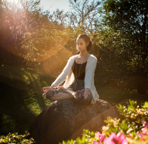 Frau meditiert im Freien mit Sonnenschein bei Kopfschmerzen